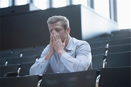 Tensed young man sitting in lecture hall by covering his face, Freiburg im Breisgau, Baden-Württemberg, Germany Stock Photo - Premium Royalty-Free, Code: 6121-08522435