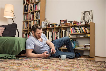 Mid adult man using digital tablet in living room, Munich, Bavaria, Germany Foto de stock - Sin royalties Premium, Código: 6121-08660274
