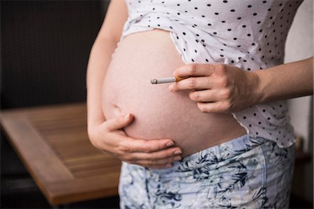 fumé - Mid section of pregnant woman holding cigarette in front of her belly, Munich, Bavaria, Germany Photographie de stock - Premium Libres de Droits, Code: 6121-08859373