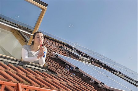 sustainable resource - Woman blowing bubbles out of roof window with solar panels Stock Photo - Premium Royalty-Free, Code: 6121-08972430