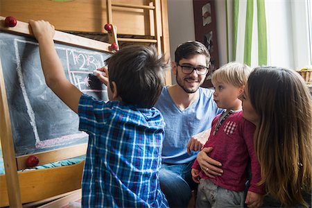 Older brother is writing on a blackboard, parents and the little brother are watching, Munich, Germany Stock Photo - Premium Royalty-Free, Code: 6121-09147051