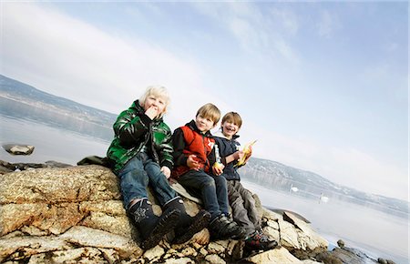 friends laughing tilted - 3 boys eating fruit at lake Stock Photo - Premium Royalty-Free, Code: 6122-07691944