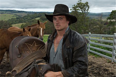 fence cowboy - horse rider holding saddle with horses Stock Photo - Premium Royalty-Free, Code: 6122-07693230