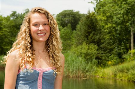 Portrait of a teenage girl smiling at camera with lake behind Stock Photo - Premium Royalty-Free, Code: 6122-07697533