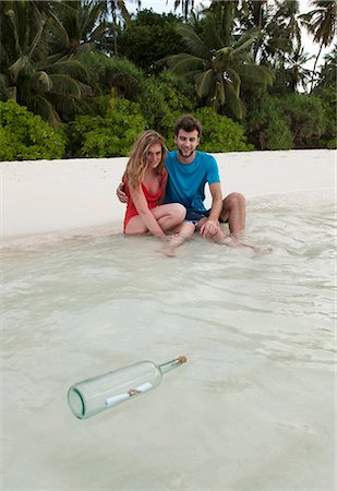 Couple at beach with message in a bottle Foto de stock - Royalty Free Premium, Número: 6122-07699018