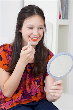 Smiling girl applying lipstick in mirror Stock Photo - Premium Royalty-Free, Code: 6122-07702353
