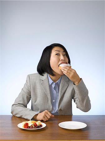 simsearch:614-02838643,k - Businesswoman eating donut at desk Photographie de stock - Premium Libres de Droits, Code: 6122-07702996
