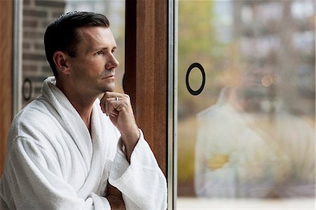 simsearch:6122-08229199,k - Man in bathrobe looking out window Foto de stock - Sin royalties Premium, Código: 6122-07703398