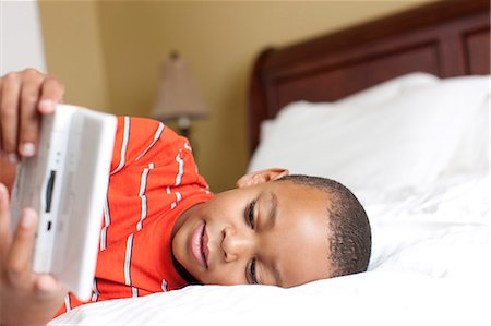 Boy playing handheld video game on bed Stock Photo - Premium Royalty-Free, Code: 6122-07704093