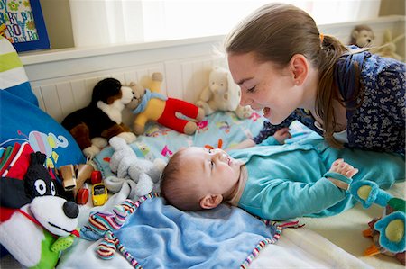 pessoa cuidando do bebê - Girl playing with baby brother on bed Foto de stock - Royalty Free Premium, Número: 6122-07704878