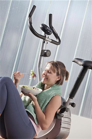 simsearch:6122-08229154,k - Woman eating salad by exercise machine Stockbilder - Premium RF Lizenzfrei, Bildnummer: 6122-07705543