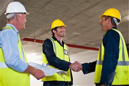 Two men wearing hard hats and hi vis vests, shaking hands