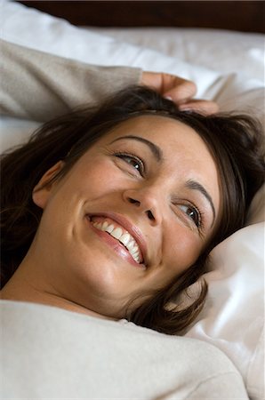 female lying on pillow arms raised images - Smiling woman laying in bed Stock Photo - Premium Royalty-Free, Code: 6122-07707073