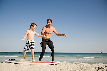 father advising son - Father teaching son how to surf Stock Photo - Premium Royalty-Free, Code: 6122-08212660