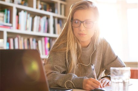 simsearch:6124-08170448,k - Teenage girl with headphones doing homework with laptop Fotografie stock - Premium Royalty-Free, Codice: 6124-08170448