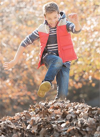 Enthusiastic boy jumping over pile of autumn leaves Stock Photo - Premium Royalty-Free, Code: 6124-08170409