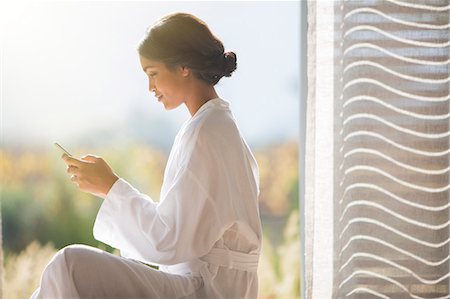 robe - Woman in bathrobe texting with cell phone in sunny doorway Stock Photo - Premium Royalty-Free, Code: 6124-08170693