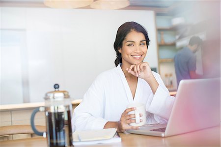 simsearch:6113-07565804,k - Portrait smiling woman in bathrobe drinking coffee at laptop Stock Photo - Premium Royalty-Free, Code: 6124-08170615