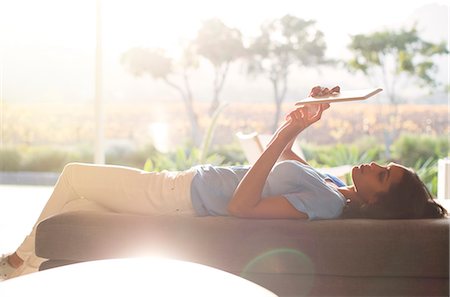 Woman laying on chaise lounge using digital tablet on sunny patio Foto de stock - Sin royalties Premium, Código: 6124-08170620