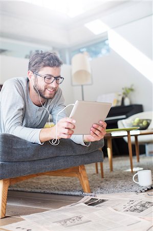 person tablet not kids - Man laying with headphones and using digital tablet in living room Stock Photo - Premium Royalty-Free, Code: 6124-08170709