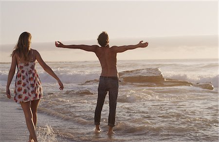 simsearch:649-03009496,k - Young woman watching exuberant young man with arms outstretched in ocean surf Photographie de stock - Premium Libres de Droits, Code: 6124-08658141