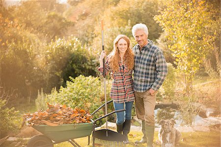 dogs leaves - Portrait smiling couple with dog gardening raking leaves in autumn garden Stock Photo - Premium Royalty-Free, Code: 6124-08820765