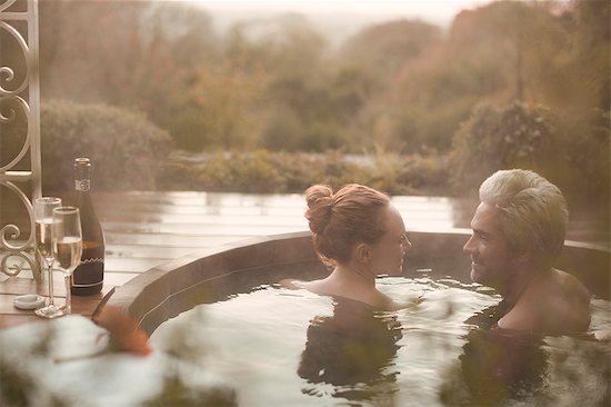 Couple talking soaking in hot tub with champagne on autumn patio Stock Photo - Premium Royalty-Free, Image code: 6124-08820770