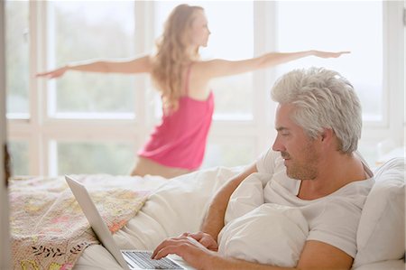 simsearch:6124-08908050,k - Woman practicing yoga warrior 2 pose in bedroom with husband using laptop in bed Fotografie stock - Premium Royalty-Free, Codice: 6124-08820721
