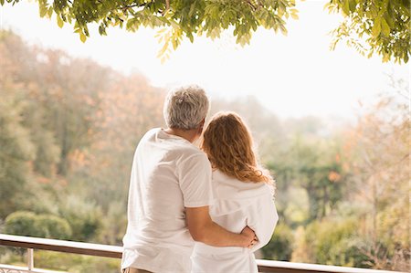 Affectionate couple hugging looking at autumn trees on patio Stock Photo - Premium Royalty-Free, Code: 6124-08820729