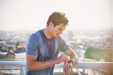 simsearch:6113-06720357,k - Sweaty male runner resting checking smart watch fitness tracker at sunny urban railing Stock Photo - Premium Royalty-Free, Code: 6124-08820857