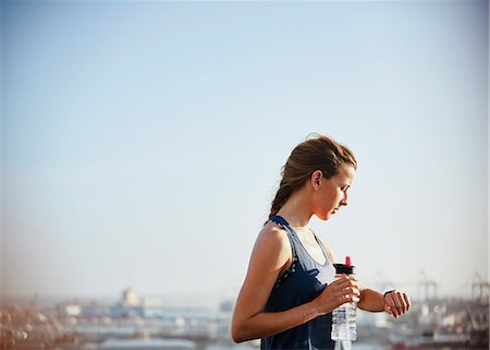 runners resting - Female runner with water bottle checking smart watch fitness tracker under sunny bleu sky Stock Photo - Premium Royalty-Free, Code: 6124-08820873