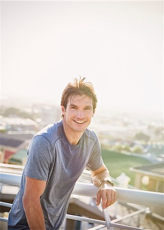 portrait of a runner - Portrait smiling male runner resting at sunny urban railing Stock Photo - Premium Royalty-Free, Code: 6124-08820875