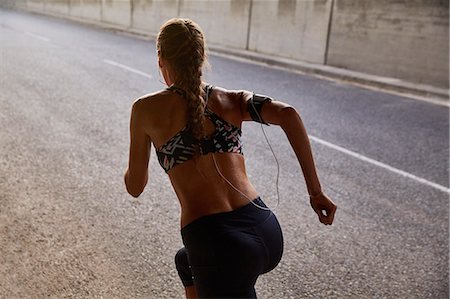 Fit female runner in sports bra and mp3 player armband running on urban street Stock Photo - Premium Royalty-Free, Code: 6124-08820819