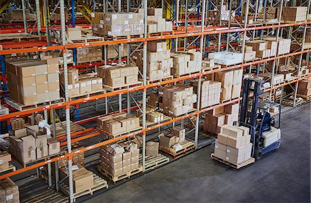 Worker operating forklift moving cardboard boxes along distribution warehouse shelves Stock Photo - Premium Royalty-Free, Code: 6124-08820946