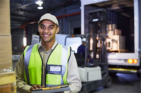 simsearch:6124-08820937,k - Portrait smiling worker in front of forklift and truck at distribution warehouse loading dock Foto de stock - Royalty Free Premium, Número: 6124-08820971