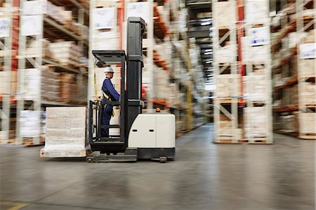 simsearch:6113-07160274,k - Worker operating forklift moving pallet of boxes in distribution warehouse Stock Photo - Premium Royalty-Free, Code: 6124-08820978