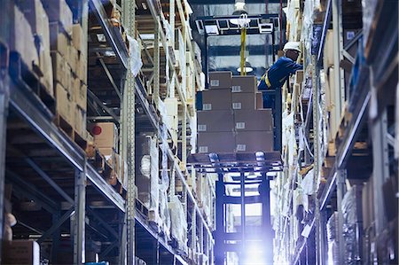 simsearch:6124-08820937,k - Worker operating forklift stacking cardboard boxes on distribution warehouse shelves Foto de stock - Royalty Free Premium, Número: 6124-08820907