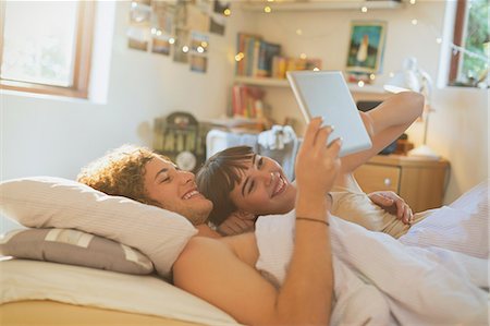 simsearch:6108-06906251,k - Smiling young couple laying in bed using digital tablet Stock Photo - Premium Royalty-Free, Code: 6124-08821093