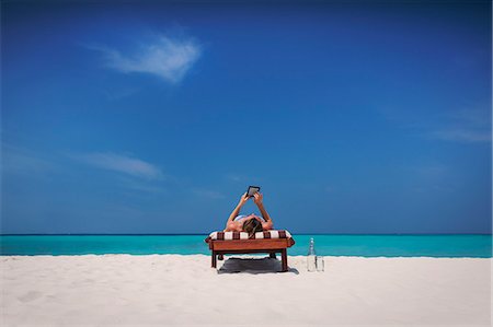 Woman relaxing, sunbathing, laying on lounge chair and using digital tablet on sunny tropical beach Photographie de stock - Premium Libres de Droits, Code: 6124-08945951