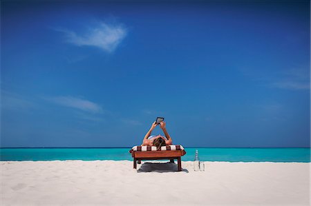 simsearch:6113-07565151,k - Woman relaxing, sunbathing, laying on lounge chair and using digital tablet on sunny tropical beach Stock Photo - Premium Royalty-Free, Code: 6124-08945951