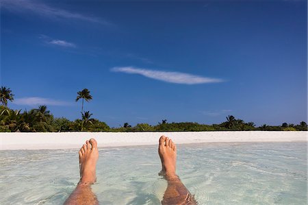 Personal perspective barefoot man floating in tropical ocean surf with view of beach Stock Photo - Premium Royalty-Free, Code: 6124-08945955
