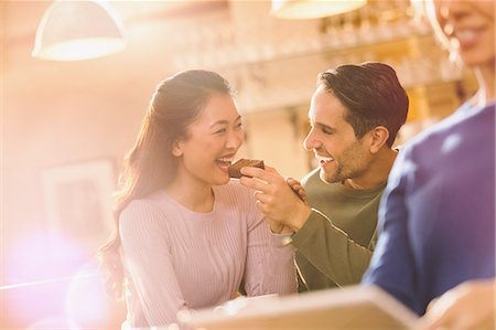 feeding food to lover images - Playful boyfriend feeding brownie to girlfriend at cafe Stock Photo - Premium Royalty-Free, Code: 6124-08946071
