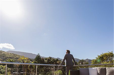 person leaning on rail with back - Businessman standing on balcony patio below sunny blue sky Stock Photo - Premium Royalty-Free, Code: 6124-08907966