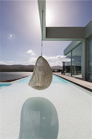 simsearch:6124-08908189,k - Hanging seat on sunny, tranquil modern luxury home showcase exterior with ocean view Stock Photo - Premium Royalty-Free, Code: 6124-08908174