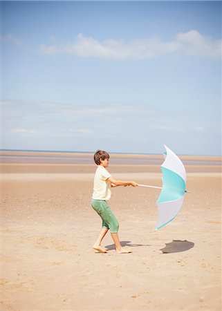 simsearch:6102-08746377,k - Wind pulling umbrella in hands of boy on sunny summer beach Stock Photo - Premium Royalty-Free, Code: 6124-08908248