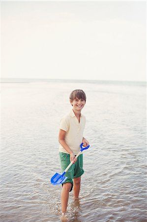 Portrait smiling boy with shovel in ocean surf on summer beach Stock Photo - Premium Royalty-Free, Code: 6124-08908268