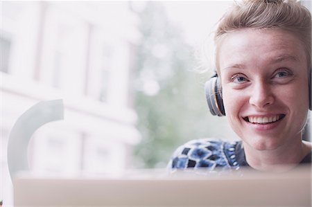 Portrait smiling young woman wearing headphones at laptop in cafe window Stock Photo - Premium Royalty-Free, Code: 6124-08926769