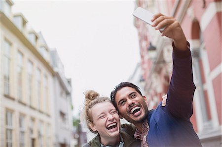 simsearch:6113-07147999,k - Enthusiastic, laughing young couple taking selfie in city Photographie de stock - Premium Libres de Droits, Code: 6124-08926821