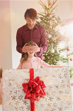 picture of man with red bow - Father covering eyes of daughter holding large Christmas gift Stock Photo - Premium Royalty-Free, Code: 6124-08926955