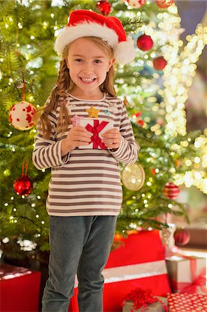 simsearch:6108-05874752,k - Portrait smiling girl in Santa hat holding gift in front of Christmas tree Photographie de stock - Premium Libres de Droits, Code: 6124-08926910